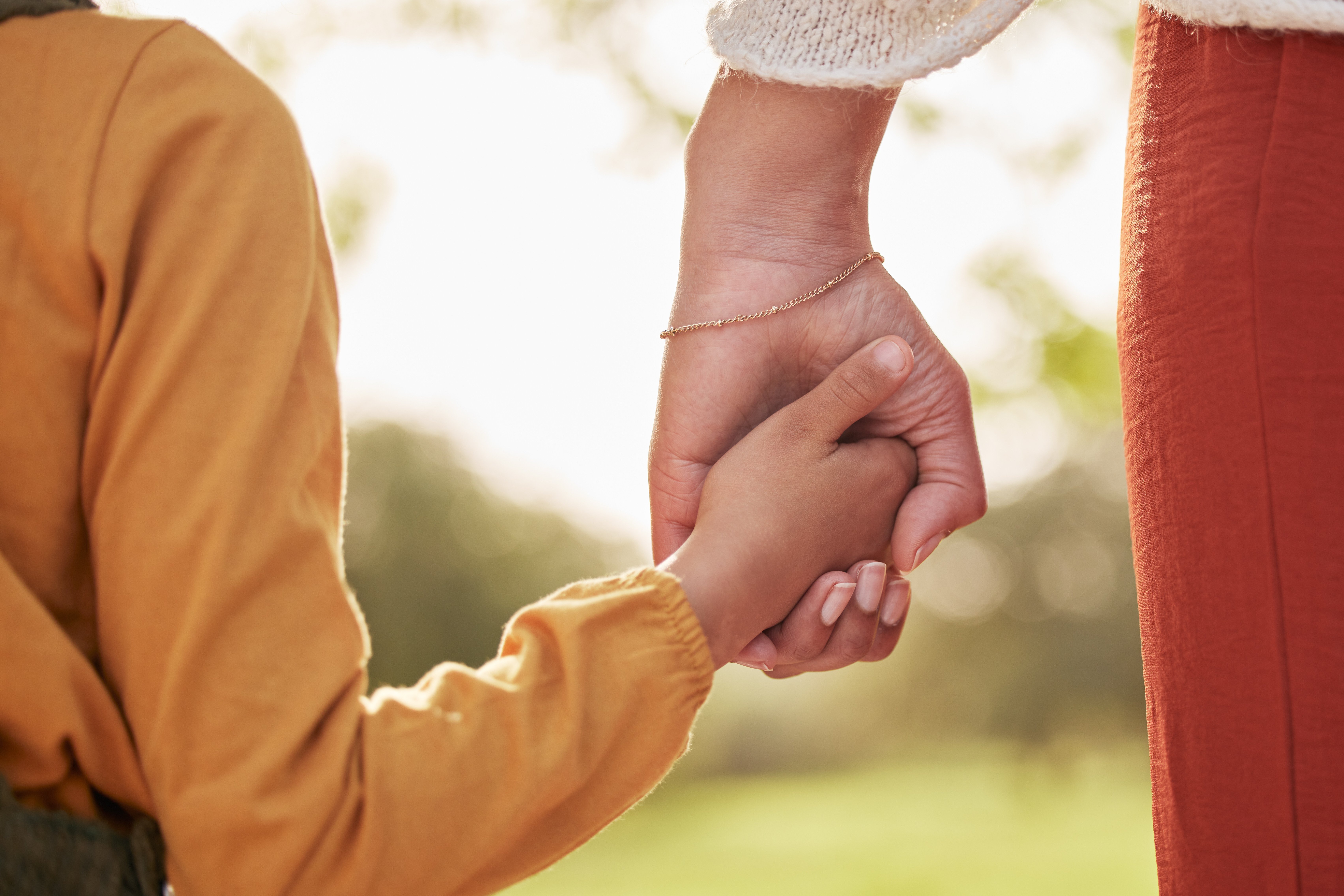 Mother, kid and holding hands for walking in park for support, trust and care together or bonding in nature. Love, comfort and parent help child in the morning sunshine with kindness on weekend